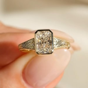 Pu&ograve; includere: Un anello in oro con una pietra centrale rettangolare taglio radiante montata in una lunetta. La fascia &egrave; realizzata in oro giallo e presenta intricati motivi a volute incisi lungo le spalle, che si estendono dalla pietra centrale.