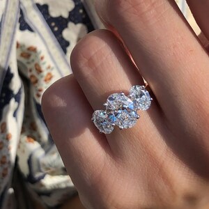 Pu&ograve; includere: Un anello a tre pietre con diamanti taglio ovale. L'anello presenta una fascia in platino o oro bianco e tre grandi diamanti scintillanti. I diamanti sono incastonati vicini, creando un'esposizione abbagliante di luce e brillantezza.