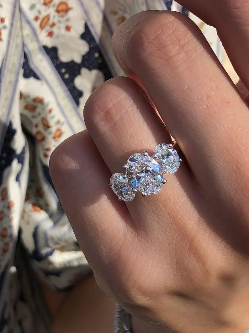 Pu&ograve; includere: Un anello a tre pietre con diamanti taglio ovale. L'anello presenta una fascia in platino o oro bianco e tre grandi diamanti scintillanti. I diamanti sono incastonati vicini, creando un'esposizione abbagliante di luce e brillantezza.