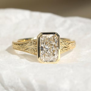 Pu&ograve; includere: Un anello in oro con una grande pietra preziosa trasparente rettangolare sfaccettata incastonata in una lunetta liscia. La fascia &egrave; realizzata in oro giallo e presenta intricati motivi a volute in rilievo sui lati, partendo dal centro.