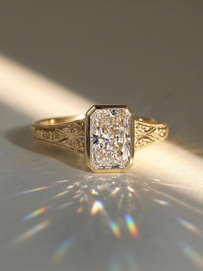 Pu&ograve; includere: Un anello in oro con una pietra centrale rettangolare taglio radiante incastonata in una lunetta liscia. La fascia in oro giallo presenta intricati motivi a volute incisi sui lati, che catturano la luce creando un effetto prismatico.