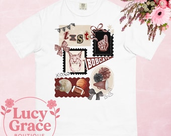 May include: White t-shirt with a collage design featuring a bobcat, football, and pom-poms. The design includes the text "txst", "BOBCATS", and "#1". The shirt has a crew neck and short sleeves.