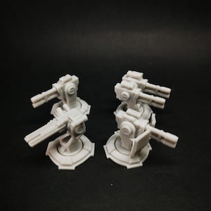 Pode incluir: Duas torres cinzentas em miniatura com vários canos, provavelmente para um jogo de tabuleiro. As torres são montadas em bases circulares e têm designs mecânicos detalhados. O fundo é preto liso.