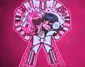 Peut inclure: Un autocollant représentant deux personnages de style anime aux cheveux roses et noirs, portant des casques et des nœuds, encadrés par une rosette circulaire avec des rubans. Le design utilise une palette de couleurs vives rose, blanc et noir.