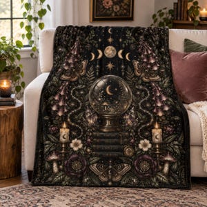 May include: A black throw blanket featuring a central crystal ball resting on a stack of books, flanked by two lit candles. The design includes moths, snakes, flowers, mushrooms, and celestial motifs like stars and moon phases in gold and purple.