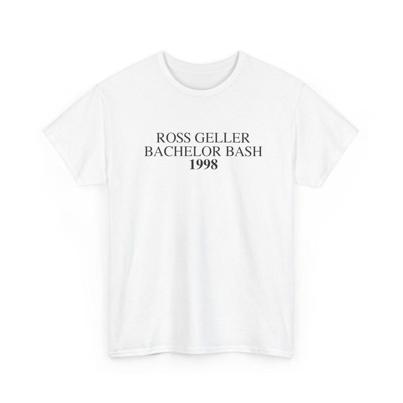 May include: A white t-shirt with the text "ROSS GELLER BACHELOR BASH 1998" printed in black. The shirt is a crew neck style and appears to be made of a soft material. The text is centered on the front of the shirt.