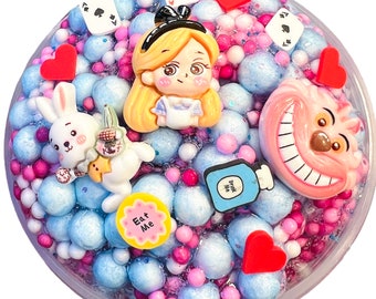 May include: Alice in Wonderland themed slime with blue, pink, and white foam balls, a white rabbit figurine, a Cheshire Cat figurine, and a bottle with "Drink Me" written on it.