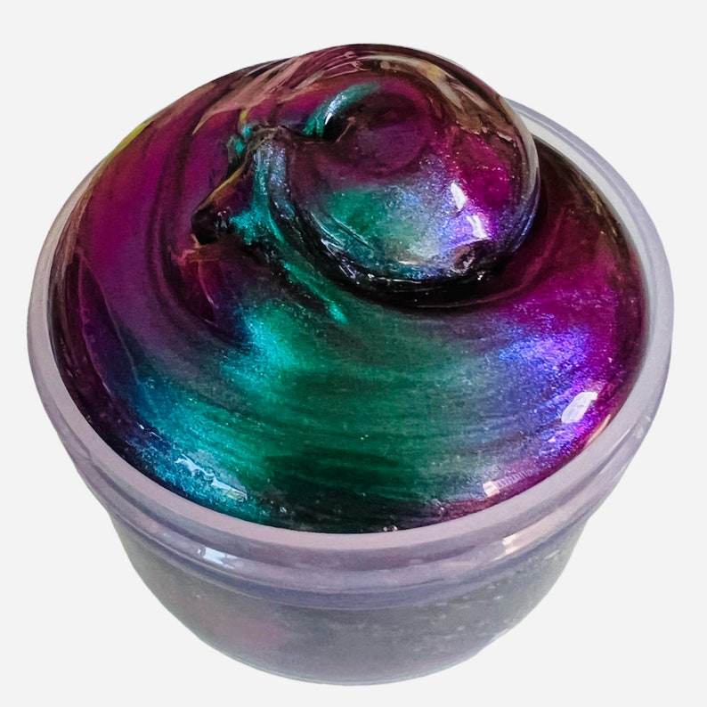 May include: A close-up of a container of iridescent slime with a swirling green and purple color.