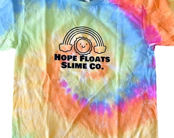 May include: A tie-dye t-shirt with a rainbow and a smiling sun graphic. The text "HOPE FLOATS SLIME CO." is printed below the graphic.