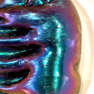 May include: A close-up of iridescent slime with a blue, green, and purple color shift. The slime is smooth and glossy, and it has a slightly textured surface.