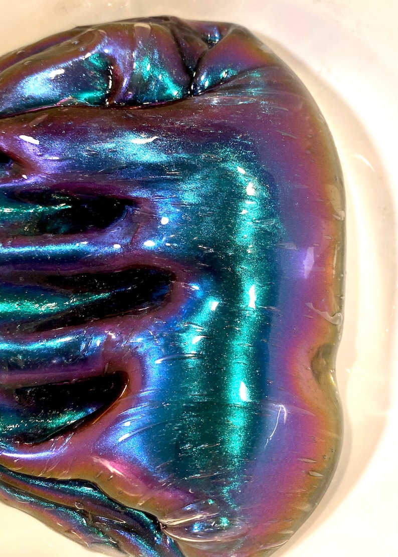 May include: A close-up of iridescent slime with a blue, green, and purple color shift. The slime is smooth and glossy, and it has a slightly textured surface.