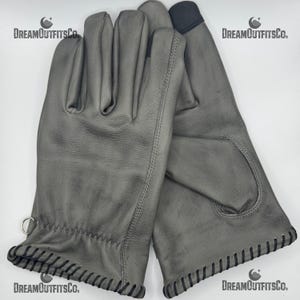 Könnte beinhalten: Ein Paar graue Lederhandschuhe mit schwarzen Nähten an den Manschetten und Nähten. Die Handschuhe haben ein fingerloses Design auf der Handflächenseite und einen kleinen Metallring am Bündchen. Der Markenname "DreamOutfitsCo." ist weiß gedruckt.