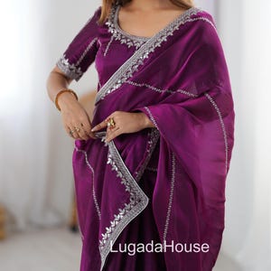 Könnte beinhalten: Ein tiefvioletter Sari mit silberner Stickerei an den Rändern und am Ausschnitt. Der Sari ist drapiert und zeigt das aufwendige Design und den fließenden Stoff. Der Text "LugadaHouse" ist auf dem Sari zu sehen.