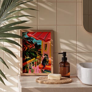 May include: A framed art print with a vibrant painting of a cat on a balcony under a red awning. The artwork is in a wooden frame, with a soap dish, soap, and a brown bottle with a black pump in front.