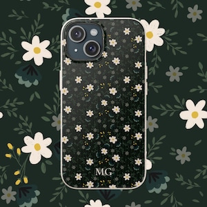 Könnte beinhalten: Schwarze Handyhülle mit weißem Rand, verziert mit einem floralen Muster aus kleinen weißen Blüten und grünen Blättern. Auf der Hülle sind die Initialen "MG" unten zu sehen. Die Kameralinsen des Telefons sind sichtbar.