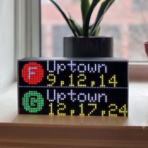May include: A rectangular digital display sign featuring two rows of LED text. The top row shows a red circle with a white F, followed by white text reading Uptown and yellow numbers 9, 12, 14. The bottom row shows a green circle with a white G, white text reading Uptown, and yellow numbers 12, 17, 24.