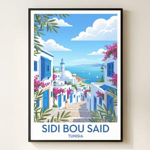 May include: A framed art print of Sidi Bou Said, Tunisia. The illustration depicts a street scene with white buildings, blue doors and windows, and vibrant pink flowers. The sky is blue with fluffy white clouds, and the text "SIDI BOU SAID TUNISIA" is at the bottom.