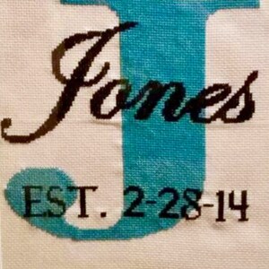 May include: Cross-stitch embroidery with the letter J in teal blue, the word "James" in black cursive, and the text "EST. 2-28-14" in black.