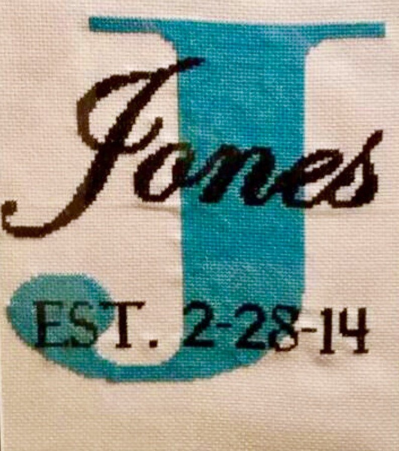 May include: Cross-stitch embroidery with the letter J in teal blue, the word "James" in black cursive, and the text "EST. 2-28-14" in black.