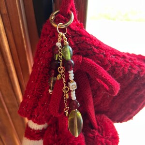 K&ouml;nnte beinhalten: Ein roter gestrickter Weihnachtsstrumpf mit wei&szlig;en Streifen und einem goldfarbenen Ring, der einen Perlenanh&auml;nger h&auml;lt. Der Anh&auml;nger hat gr&uuml;ne, rote und wei&szlig;e Perlen und eine kleine goldfarbene Kette.