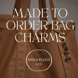 Puede incluir: Un bolso tote marr&oacute;n con un charm decorativo. El bolso tiene un bolsillo y correas largas. El texto de la imagen dice "MADE TO ORDER BAG CHARMS" y "ANN & ELLIOT CO."