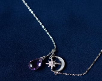 May include: A silver necklace with celestial charms. The necklace features a teardrop-shaped purple gemstone, a crescent moon, and a star pendant. The chain is delicate, and the charms are detailed, set against a dark blue background.
