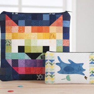 May include: Two zippered pouches. The larger pouch features a colorful patchwork cat face design. The smaller pouch has a white background with a blue abstract cat and geometric patterns. Both have black zippers.
