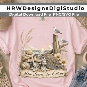 May include: A light pink t-shirt featuring a graphic of a sea turtle wearing a striped bow, stacked seashells, two seagulls perched on a piece of driftwood, and flowers. The text "slow down, soak it in" is printed at the bottom of the design.