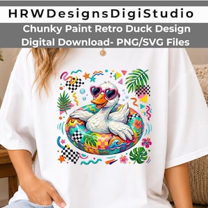 May include: A white t-shirt featuring a graphic of a white duck wearing pink heart-shaped sunglasses while floating in a colorful, patterned inner tube. The design includes tropical leaves, checkered squares, and abstract shapes in bright colors.