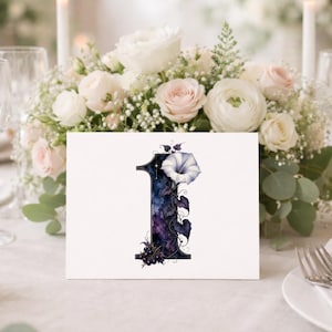 K&ouml;nnte beinhalten: Eine wei&szlig;e, rechteckige Tischkarte mit der Zahl Eins in einem dunkelblauen und violetten Aquarell-Galaxie-Muster. Die Zahl ist mit einer einzelnen wei&szlig;en Prunkwinde, dunkelgr&uuml;nen Bl&auml;ttern und kleinen dunklen Beerenclustern verziert.