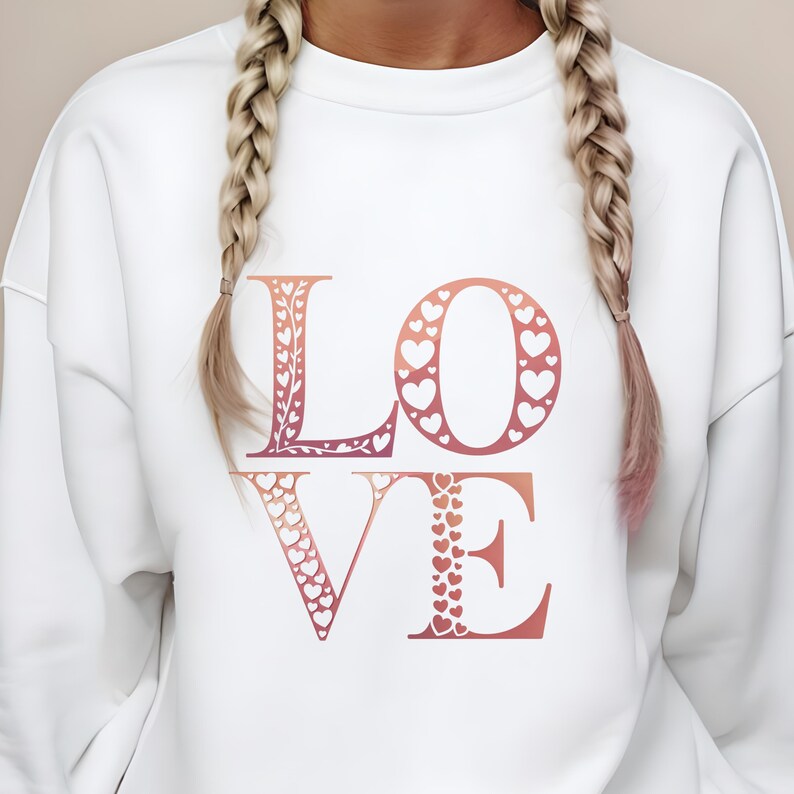 Op de afbeelding: Witte sweatshirt met het woord "LOVE" in een roze en oranje gradi&euml;nt. De letters zijn versierd met hartvormige uitsparingen en bloemmotieven. Een casual, romantisch ontwerp.