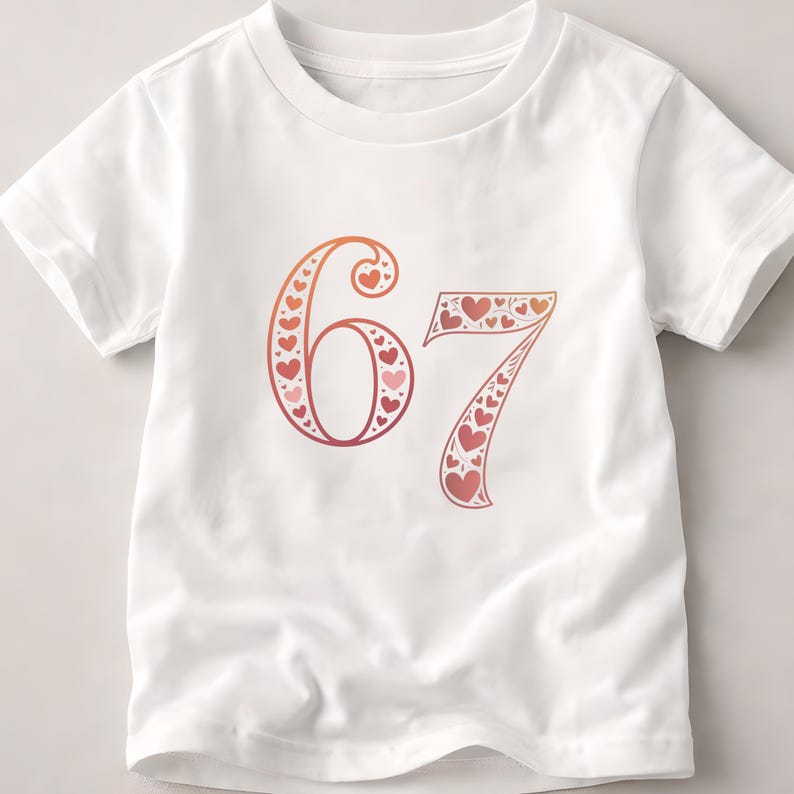 Op de afbeelding: Wit T-shirt met het nummer 67 in een rood-oranje verloop, gevuld met hartvormen. Het shirt heeft korte mouwen en een ronde hals.