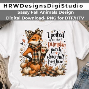 May include: A white t-shirt featuring a graphic of a fox wearing a leopard print bow and a plaid scarf, holding a mug. The text reads, I peaked at the pumpkin patch, downhill from here. The design includes pumpkins, autumn leaves, and small hearts.