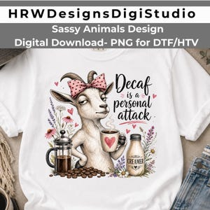 May include: A white t-shirt featuring a graphic of a goat wearing a pink polka-dot bow, holding a coffee mug with a red heart. The text reads Decaf is a personal attack. Includes a French press, coffee beans, a creamer bottle, and floral accents.