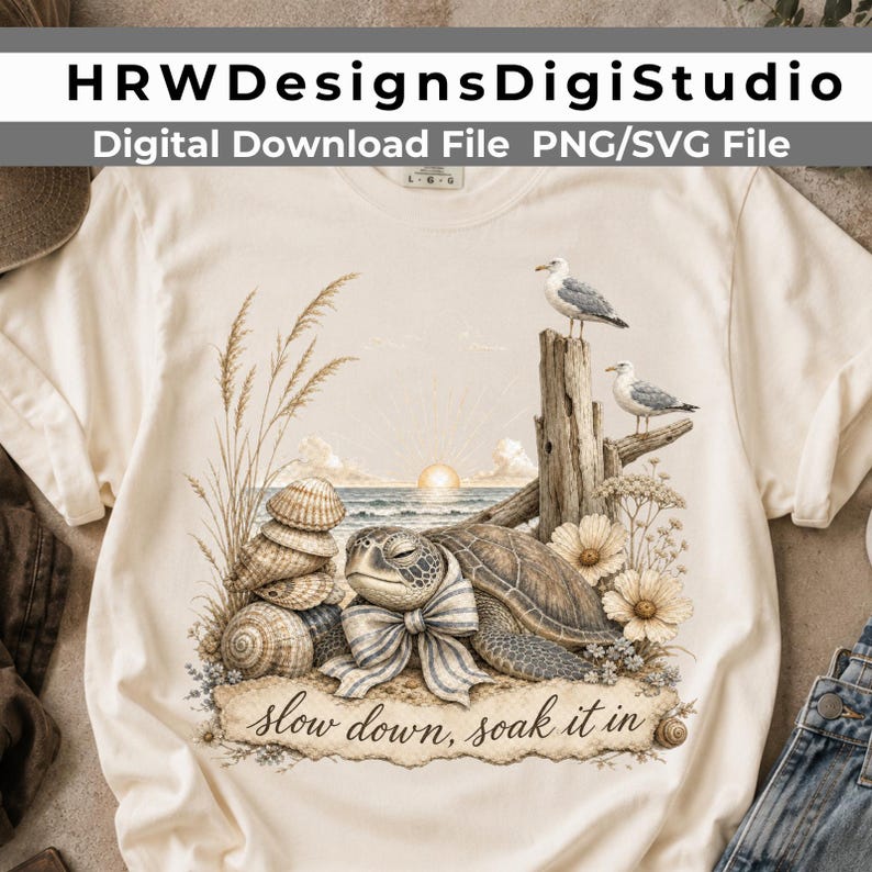 May include: A cream-colored t-shirt featuring a graphic of a sea turtle wearing a striped bow, stacked seashells, tall beach grass, two seagulls perched on driftwood, and a sunrise over the ocean with the text, "slow down, soak it in."