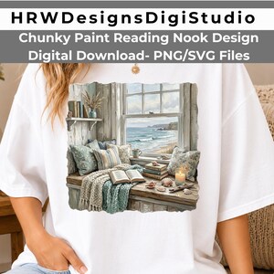 Könnte beinhalten: Ein weißes T-Shirt mit einem Grafikdruck einer gemütlichen Leseecke am Fenster mit Blick auf das Meer. Die Illustration zeigt eine Fensterbank mit Kissen, einer Strickdecke, einem aufgeschlagenen Buch, Bücherstapeln, Muscheln und einer brennenden Kerze.