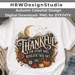 Puede incluir: Una camiseta blanca con un estampado gráfico que muestra una luna creciente, estrellas, hojas de otoño, trigo y calabazas. El texto dice: THANKFUL FOR EVERY SOUL BENEATH THIS SKY. El diseño incluye remolinos intrincados y elementos celestiales.