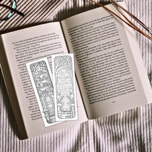 May include: Two black and white bookmarks with a fantasy theme, featuring a bookshelf, trees, and a door. The bookmarks are placed on an open book with text.
