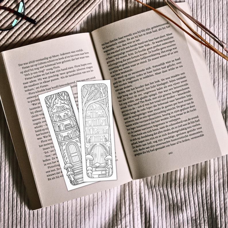 May include: Two black and white bookmarks with a fantasy theme, featuring a bookshelf, trees, and a door. The bookmarks are placed on an open book with text.