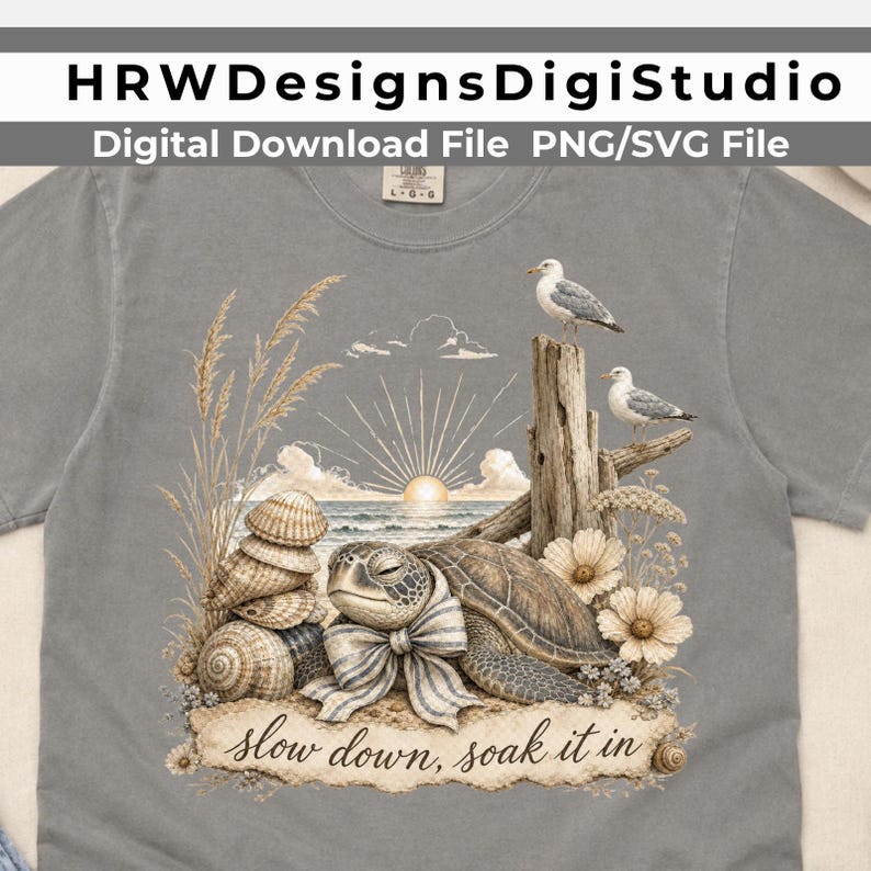 May include: A gray t-shirt featuring a graphic of a sea turtle wearing a striped bow, stacked seashells, two seagulls on a wooden post, and tall grass. The scene includes a sunrise over the ocean and the text "slow down, soak it in" at the bottom.