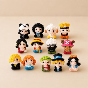 May include: A collection of fourteen small, handcrafted crochet dolls featuring various character designs with distinct outfits, hair colors, and accessories, including hats, masks, and colorful yarn details, arranged in three rows on a plain surface.