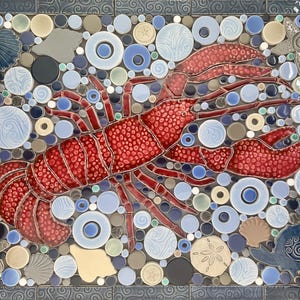 May include: A rectangular tile mosaic featuring a large red lobster surrounded by various sea-themed elements. The design includes seashells, starfish, and bubbles in shades of blue, gray, and beige, all set against a dark blue border.
