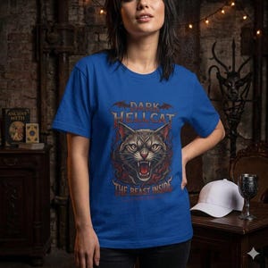 May include: A royal blue short-sleeve t-shirt featuring a graphic print of a snarling cat face surrounded by red flames and bat silhouettes. The text reads DARK HELLCAT at the top and THE BEAST INSIDE at the bottom in a stylized font.