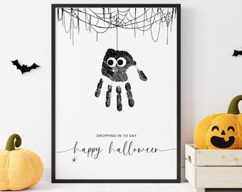 May include: Black framed Halloween art print featuring a handprint spider with googly eyes, a spiderweb, and the text "Dropping in to say happy Halloween". Decorative bats and pumpkins complete the festive scene.