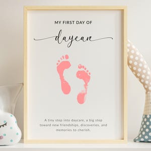 May include: Framed print with the text "MY FIRST DAY OF daycare" in black script above two pink footprint impressions. Below the footprints is the text: "A tiny step into daycare, a big step toward new friendships, discoveries, and memories to cherish."