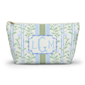 May include: A rectangular cosmetic bag with a gold zipper, featuring a floral and striped pattern in white, light blue, and green. The bag has a central light blue frame with the monogram "LGM" in a matching light blue font.