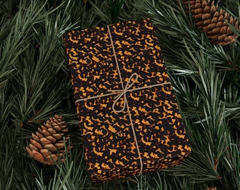 May include: A wrapped gift with a brown and yellow tortoiseshell pattern, tied with twine, rests on a bed of green pine needles. Several pine cones are scattered around the gift, creating a festive holiday scene.