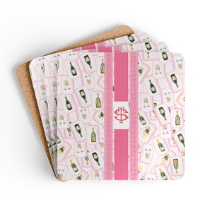 Pode incluir: Conjunto de quatro bases quadradas com verso em cortiça. As bases apresentam um padrão rosa e branco de garrafas e taças de champanhe. Uma faixa rosa vertical com um monograma vermelho é centralizada nas bases.