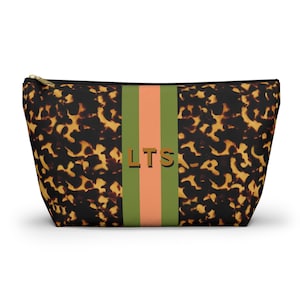 May include: A zippered pouch featuring a brown and black tortoiseshell pattern. A vertical stripe runs down the center in olive green and peach, with the letters LTS printed in a dark brown serif font centered within the stripe.