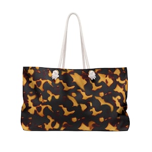 Può includere: Una grande borsa tote con un motivo a scaglie di tartaruga nei toni del marrone e del giallo. La borsa ha manici in corda bianca e dettagli bianchi agli angoli superiori. La borsa è rettangolare e sembra essere realizzata in un materiale resistente.